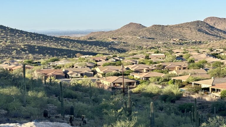 An aerial view looking over luxury desert homes nestled into the mountainside of the Hidden Hills neighborhood in Scottsdale, Arizona, demonstrating high property values.